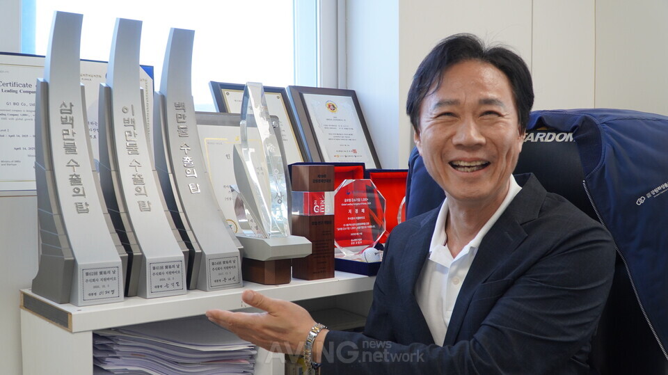 김우식 지원바이오 대표가 춘천 본사 집무실에서 백만불·이백만불·삼백만불 수출의 탑을 가리키고 있다. 지원바이오는 2017년 백만불 수출의 탑을 시작으로 2024년 이백만불, 2025년 삼백만불 수출의 탑을 잇달아 수상하며 성장세를 이어가고 있다. | 촬영 - 에이빙뉴스